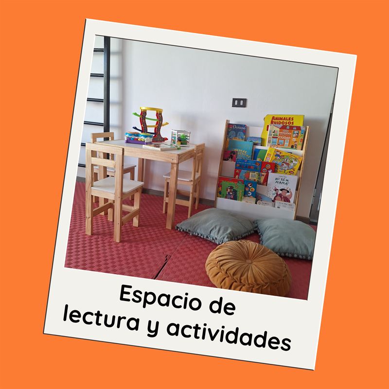 Espacio de lectura y actividades: mesa y sillas de madera, repisa con cuentos y cojines sobre piso de goma.